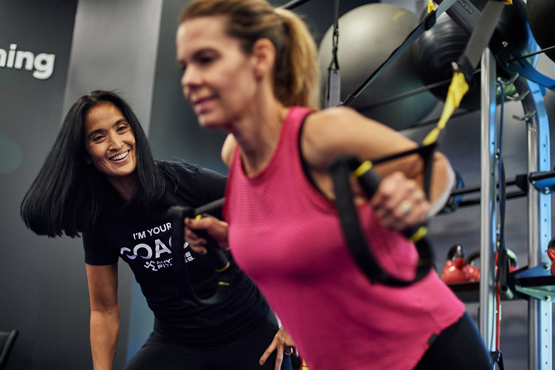 A woman doing a chest press with suspension straps receiving encouragement from her coach